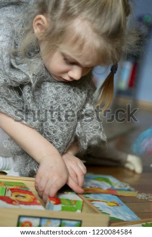 blonde girl in a gray shawl collects a picture of animals from cubes sitting on the floor