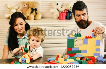 Mom, dad and boy on wooden background build out of plastic blocks. Young family spends time in playroom. Family and childhood concept. Parents and son with concentrated faces make brick constructions.