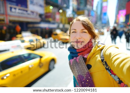 Happy young woman tourist sightseeing at Times Square in New York City. Female traveler taking selfies with her smartphone in downtown Manhattan. Travelling in USA.