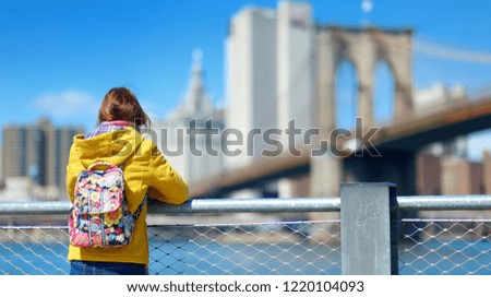 Happy young woman tourist sightseeing by Brooklyn Bridge, New York City, at sunny spring day. Female traveler enjoying view of downtown Manhattan. Travelling in USA.