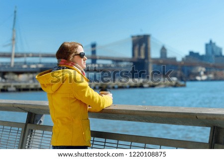 Happy young woman tourist sightseeing in New York City at sunny spring day. Female traveler drinking coffee in downtown Manhattan. Travelling in USA.
