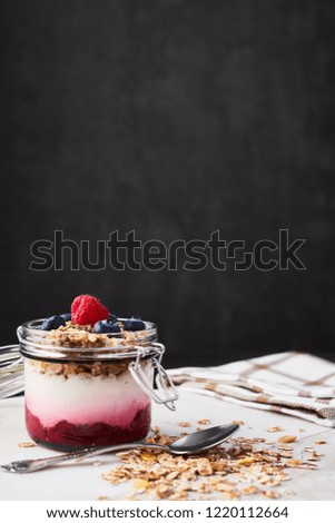 Healthy breakfast. Jar of healthy yogurt with raspberry sauce, oat and blueberries on white marble serving plate over dark concrete background with copy space.