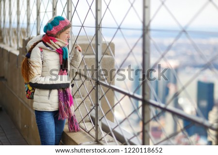 Happy young woman tourist at the observation deck of Empire State Building in New York City. Female traveler enjoying the view of NYC skyline. Travelling in USA.