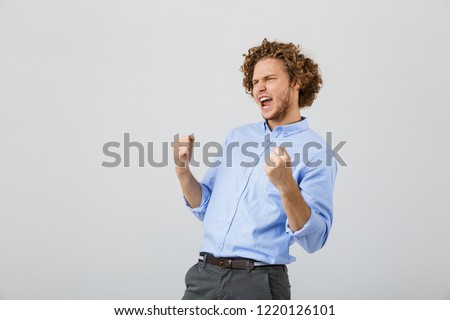 Portrait of a happy young man wearing shirt standing isolated over gray background, celebrating success