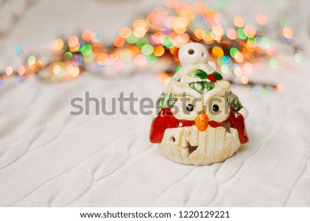 souvenir owl on a white knitted plaid on the background of colorful lights, Christmas card, copy space