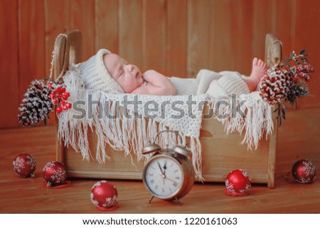 A newborn baby is lying in a small bed decorated with balls, cones and a clock / copy space