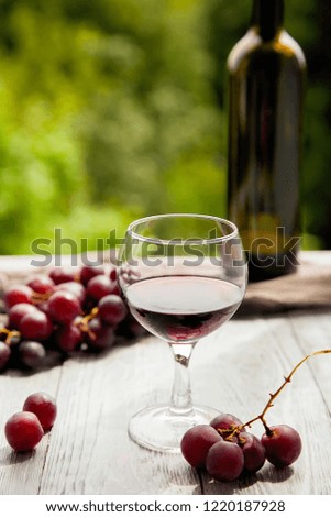 Red wine bottle, one glass,red grape on wooden and nature background