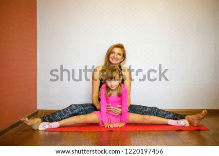Mom and daughter do exercises on the mat. Mom with a child on a yoga mat smiling and sitting on the splits. Health family doing pilates.