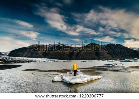 Woman in yellow raincoat standing at icebergs in arctic ocean near Vatnajokull National Park in Iceland. Royalty-Free Stock Photo #1220206777