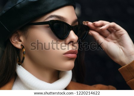 Outdoor close up fashion portrait of young beautiful woman wearing cat eye sunglasses, leopard print hoop earrings, leather beret. Model looking aside