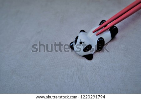 Cute Panda chopsticks holder stand, ceramic chopsticks rest with red chopsticks on grey background. It can rest spoon fork knife.This is Chinese and Asian meal culture.
