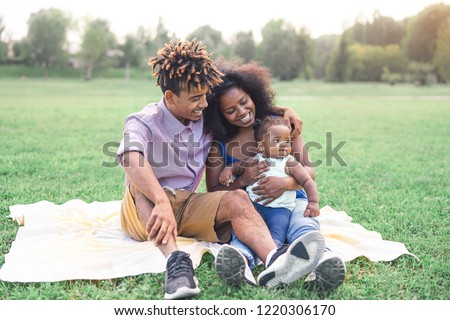 Happy black family doing a picnic outdoor - Mother and father having fun with their daughter in a park - Love and happiness concept 