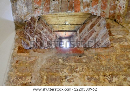 A small narrow window on an old, ancient, cracked stone shabby brick wall of red brick in the basement. The background.