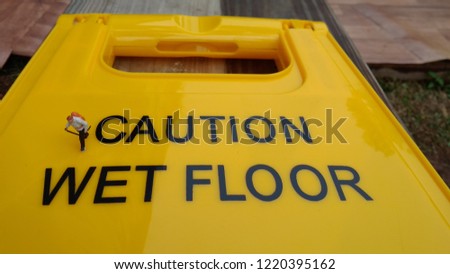 miniature figure adventurer walking at big yellow caution wet Floor sign