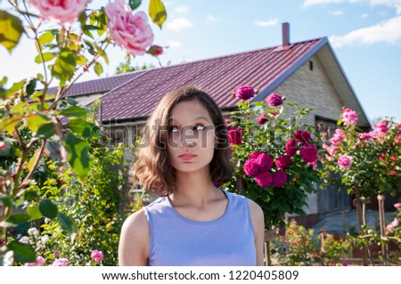 Portrait of a beautiful brunette in red rose bushes at summer cottage