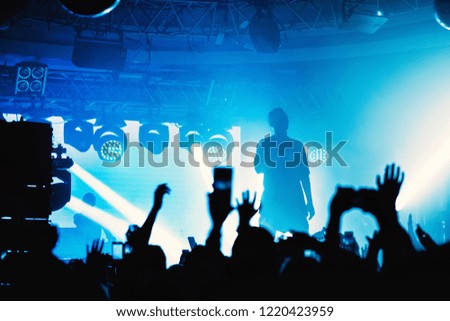 DJ  at the main stage hands up with crowd of people in night club party under light