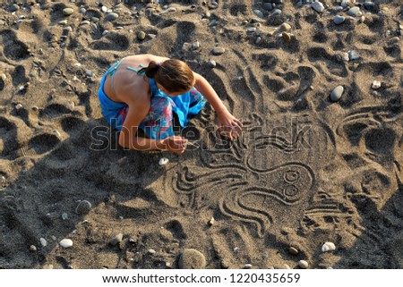 Girl draws on the sand.