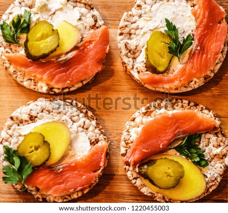 Sandwiches on a wooden background. Sandwich with red fish and curd cheese, ginger, pickled cucumber and parsley on a cereal loaf. Dietary nutrition.
