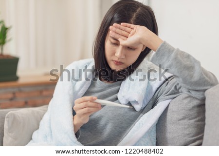 Young Asian woman have a cold and high fever while checking body temperature by using digital thermometer. Royalty-Free Stock Photo #1220488402