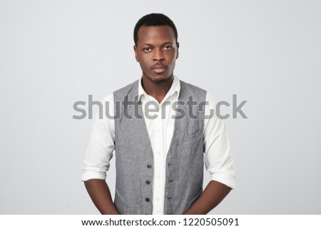 Thinking black afro american man with serious expression looking into camera while posing against white studio wall. Grave businessman in white and vest shirt thinking about work