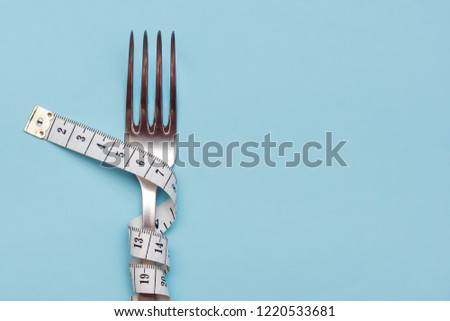 Measuring tape wrapped around a fork lying on a blue background. Proper nutrition. Medical starvation. Diet for weight loss concept. Free space for text or advertisement. Royalty-Free Stock Photo #1220533681