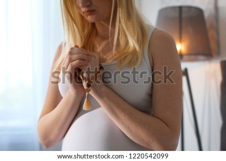 Young pregnant woman with beads praying indoors