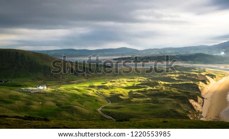 A ray of sun light breaks through the clouds to cast light on to a small white church. This is a picture of Five Finger Stand beach and sand dunes in Donegal Ireland