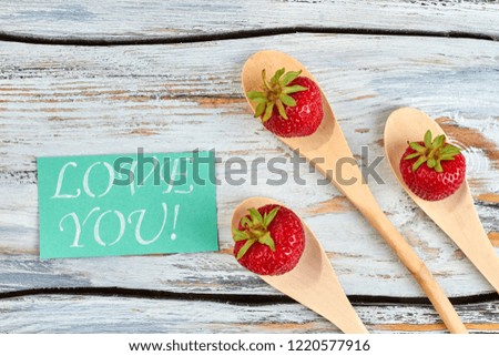 Ripe juicy strawberries in wooden spoons. Delicious strawberries on wooden background and card with text for you, top view.