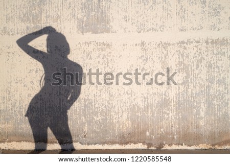 Silhouette of anonymous woman posing over weathered concrete wall on sunny day. She is holding arm on her head.