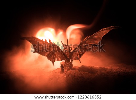 Silhouette of fire breathing dragon with big wings on a dark burning fire background. Selective focus