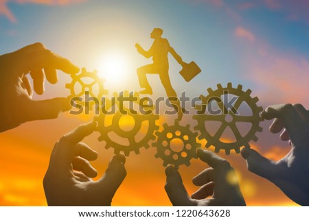 human silhouette businessman with a briefcase running gears for transmissions in the hands of four people on a background of the sky with the sun glare. Business concept idea, teamwork.