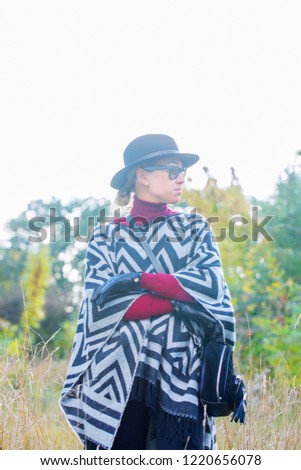 Beautiful woman in poncho hat and gloves is walking in the park