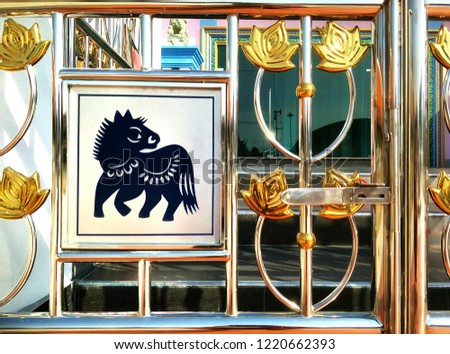Part of the old vintage stainless steel gate with gold leaf pattern and horse Chinese zodiac sign in front of Thai temple pavilion on architecture design concept, close up shot with blur background 