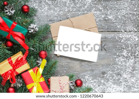christmas greeting card with fir branches, gift boxes, red decorations and pine cones on rustic wooden table covered with snow. Christmas background. Flat lay. top view with copy space