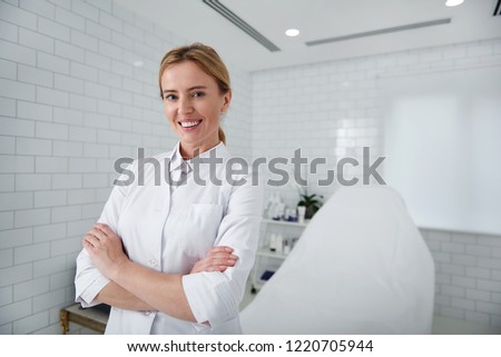Welcome to our salon. Waist up portrait of charming beautician in white lab coat looking at camera with smile