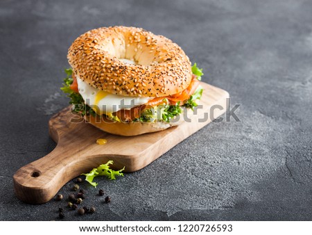 Fresh healthy bagel sandwich with salmon, ricotta and soft egg on vintage chopping board on stone kitchen table background Royalty-Free Stock Photo #1220726593