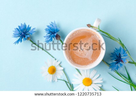 Spring background. Cornflowers, chamomile and a cup of hot coffee on a blue background. Top view 