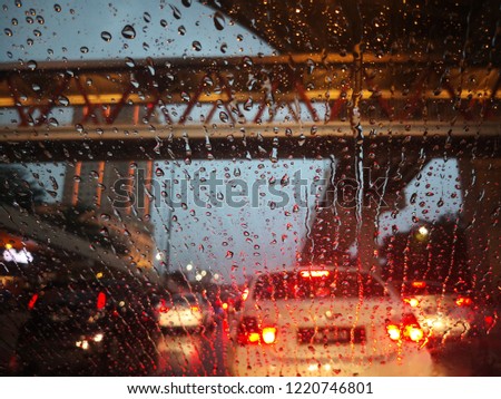 Rain drops on window with road light bokeh, City life in night in rainy season abstract background,water drop on the glass, night storm raining car driving concept.

