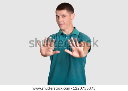 Waist up shot of handsome man demonstrates refusal gesture, asks not bother him, rejects something, has displeased facial expression, dressed in casual clothes, isolated over white studio wall Royalty-Free Stock Photo #1220755375