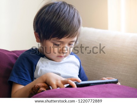 Cute little boy watching cartoons on digital taplet,Preschool kid sititng on sofa with serious face playing games on touch pad, Child relaxing at home.
