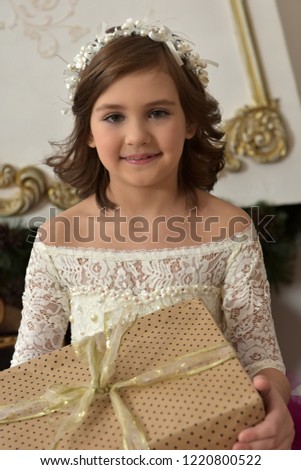 a girl in a chic white with a burgundy dress with a golden box with a gift in her hands
