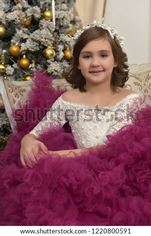 a girl in a chic white dress with a burgundy dress sits on a sofa in a room with Christmas decorations