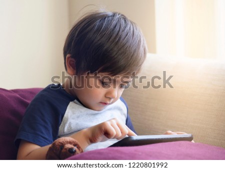 Cute little boy watching cartoons on digital taplet,Preschool kid sititng on sofa with serious face playing games on touch pad, Child relaxing at home.