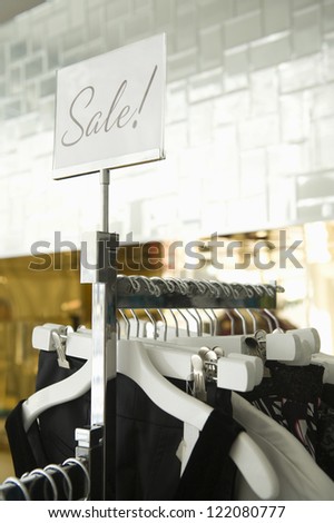 Clothing hanging on a rack in fashion retail store with "SALE" sign on the plate