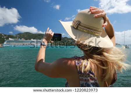 Beautiful woman in hat take picture from mobile phone of Luxury Cruise Liner hobart in the port in tropical island in summer time