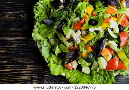 Greek salad with fresh cucumbers, tomatoes, sweet peppers, lettuce, red onions, feta cheese and olives with olive oil on a dark wooden background.