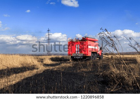Red firetruck car Ural rides through the autumn field with yellow and faded grass against the blue sky and clouds. The concept of extinguishing forest fires in California