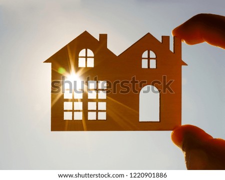 Male hand holding a wooden toy house with window and door against blue sunny sky. sun rays, beam. sun light. eco bio building