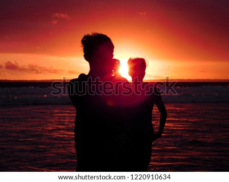 a silhouette of a young man taking picture of another young man in a beach on sunset time.