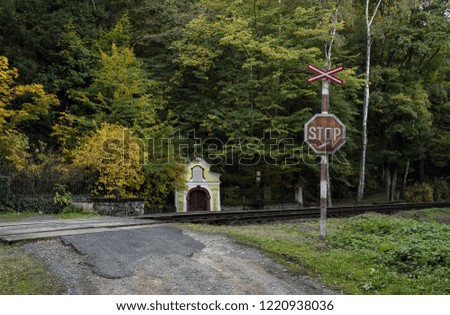 a railway crossing with a trail mark and a small yellow chapel in the woods